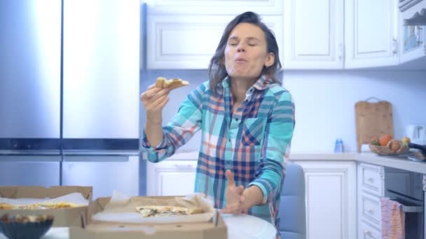 Wesoła zabawna kobieta jedząca pizzę z pudełka w domu w kuchni — Wideo stockowe
