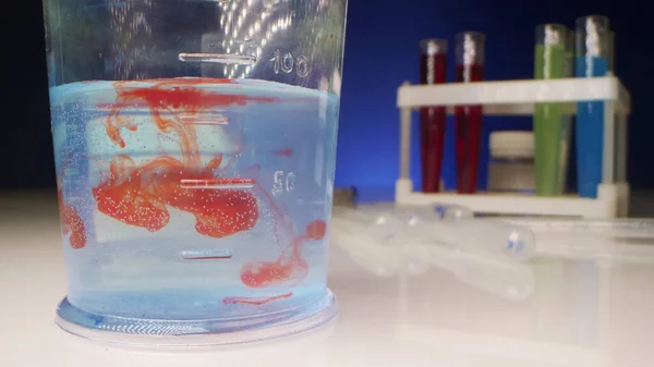 Eksperimen kimia. cairan merah larut dalam cairan yang jernih dalam tabung percobaan — Stok Foto