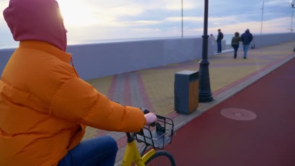 Ceketli bir kadın deniz kenarında bisiklet sürüyor. — Stok video