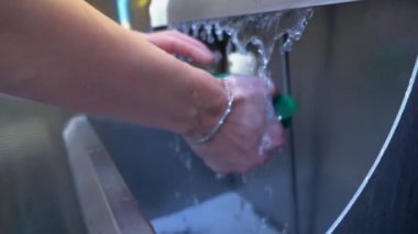 Endüstriyel bir lavaboda büyük bir süngeri durulayan kadın ellerinin yakın çekimi.