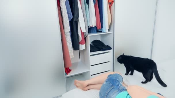 Een vrouw rust op een bed met een kat tegen de achtergrond van een open kledingkast — Stockvideo
