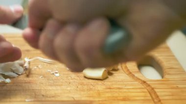 Erkek ellerinin tahta kesme tahtasıyla sarımsak keserken yakın plan çekimleri.