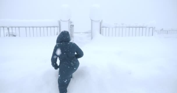 Uma mulher faz seu caminho através dos snowdrifts para entrar no portão — Vídeo de Stock