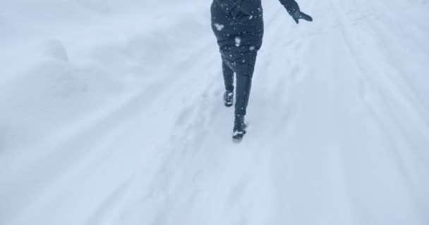 Женщина в пальто идет по пустынной заснеженной дороге через снежные заносы — стоковое видео