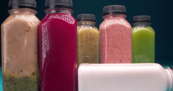 Detallado primer plano extremo de un conjunto de botellas con zumos de frutas y verduras multicolores sobre un fondo azul — Vídeos de Stock