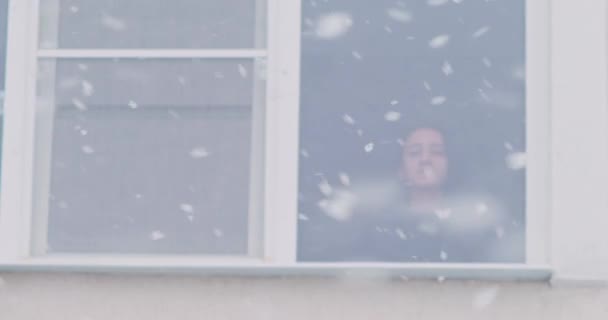 Kar fırtınası sırasında kız pencereden dışarı bakar. Sokağın manzarası — Stok video