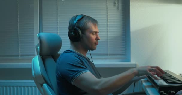 Мужчина в наушниках пишет музыку, играющую на клавиатуре midi в студии звукозаписи — стоковое видео