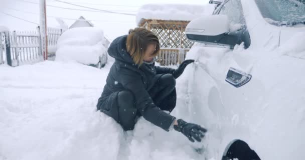 Жінка очищає машину від снігу руками, кліматична аномалія — стокове відео