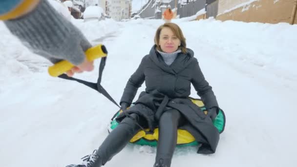 Diversión invernal. alguien está tomando una mujer sonriente en un trineo inflable de la montaña — Vídeos de Stock