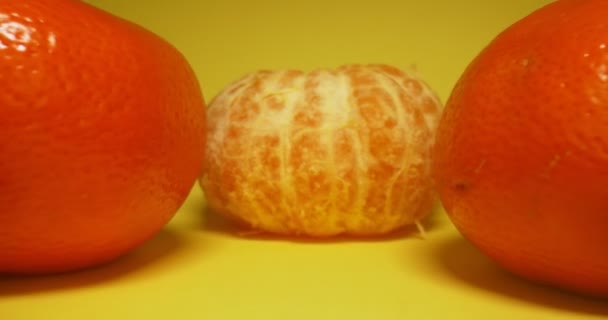 Detallado primer plano extremo de un grupo de mandarinas, una de las cuales es pelada, fondo amarillo — Vídeos de Stock