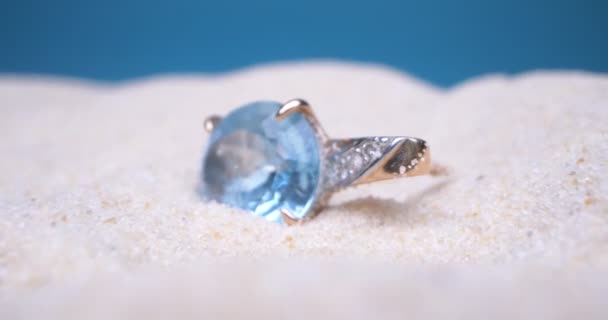 Деталізована екстремальна крупним планом, золота сережка з блакитним топазом і діамантом на білому піску — стокове відео