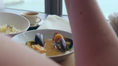 close-up, someone eats tom yam with mussels with a spoon from a white plate