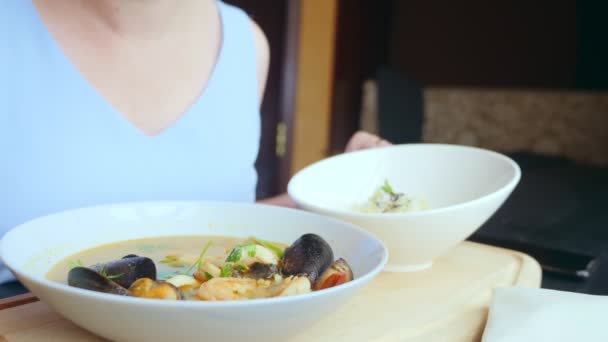 Nahaufnahme, jemand isst Tomyam mit Muscheln mit einem Löffel von einem weißen Teller — Stockvideo