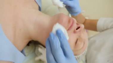 kauçuk eldivenli güzellik uzmanının elleri kadınların yüzlerini peçetelerle temizler.