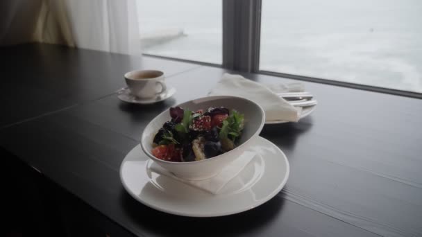 Gros plan d'un plat d'aubergines cuites au four avec des tomates sur la table près de la fenêtre donnant sur la mer — Video