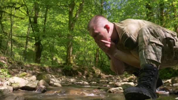 Super-Slow-mo. Mann in khakifarbener Uniform wäscht sein Gesicht aus einem Waldbach mit Wasser — Stockvideo