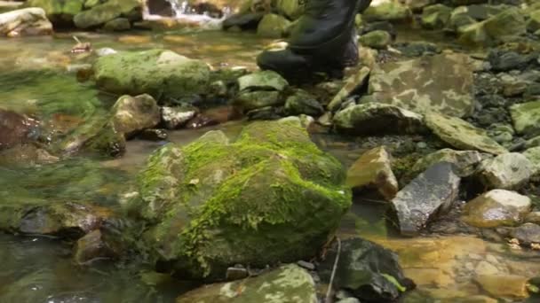 特写。脚穿脚踝靴的人跨入山溪，穿过山溪进入浅滩 — 图库视频影像