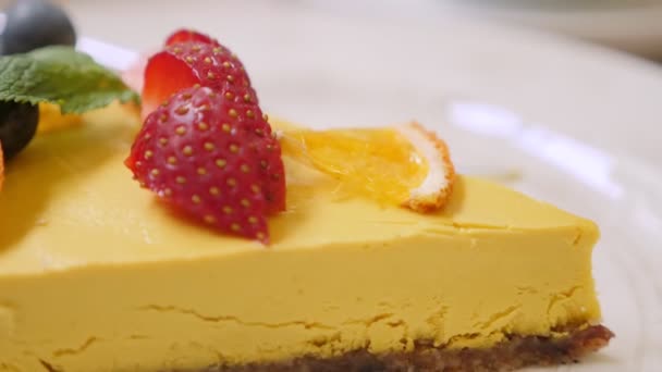 Крупный план ломтика сырого манго пассионфруктовый торт украшенный клубникой и черникой — стоковое видео