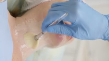 Yakın plan. Güzellik uzmanı bir kadının yüzüne fırçayla maske takar.