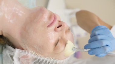 dikey video. Yakın plan. Güzellik uzmanı bir kadının yüzüne fırçayla maske takar.