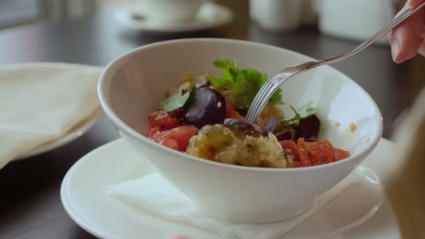 Close-up. vrouw eten gebakken aubergine met tomaten terwijl zitten aan de tafel aan het raam met uitzicht op de zee — Stockvideo