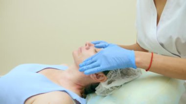 Yakın plan. Lastik eldivenli bir güzellik uzmanının elleri kadın bir hastanın yüzüne krem sürer.