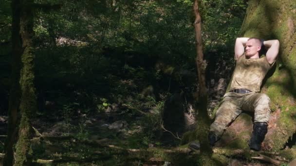 Ένας άντρας με στολή χακί αναπαύεται στο δάσος κάτω από ένα δέντρο. — Αρχείο Βίντεο