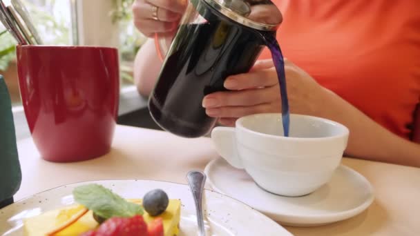 Primer plano. mujer irreconocible vierte té azul de una tetera mientras está sentado en una mesa en un café — Vídeos de Stock