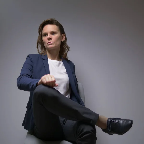 Cool business woman in a jacket sitting in a chair on a dark background — Stok Foto