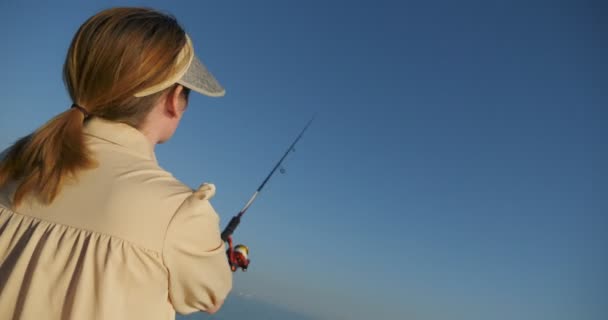 Beautiful woman in a dress fishing with a spinning rod in the sea — Stock Video