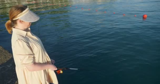 Hermosa mujer en un vestido de pesca con una caña de spinning en el mar — Vídeo de stock