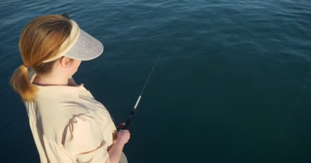 Bela mulher em um vestido de pesca com uma vara de fiação no mar — Vídeo de Stock