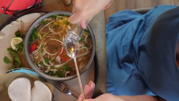 Närbild ovanifrån. kvinnliga händer lägga till sås till en skål med pho bo soppa — Stockvideo