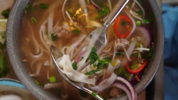 Nahaufnahme von oben, jemand isst Pho Bo Suppe mit Gabel und Löffel von einem großen Teller — Stockvideo