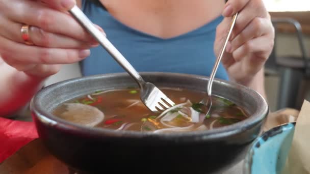 Zbliżenie, kobieta w niebieskim jedząca zupę pho bo z widelcem i łyżką z dużego talerza — Wideo stockowe