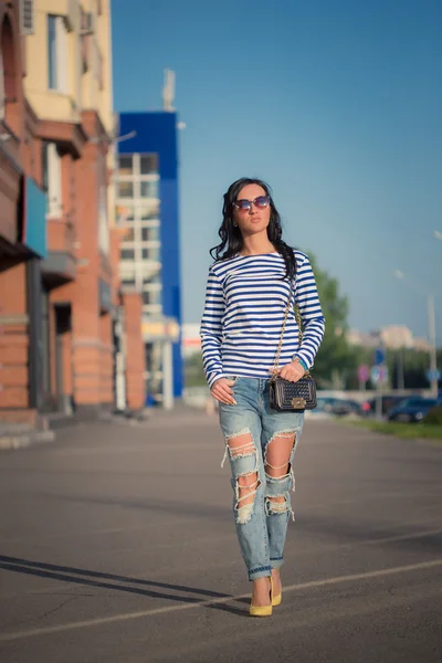 Schöne brünette Mädchen geht durch die Straßen der Stadt. in zerrissenen Jeans und Gehrock — Stockfoto