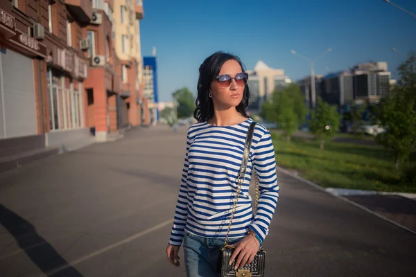 Schöne brünette Mädchen geht durch die Straßen der Stadt. in zerrissenen Jeans und Gehrock — Stockfoto