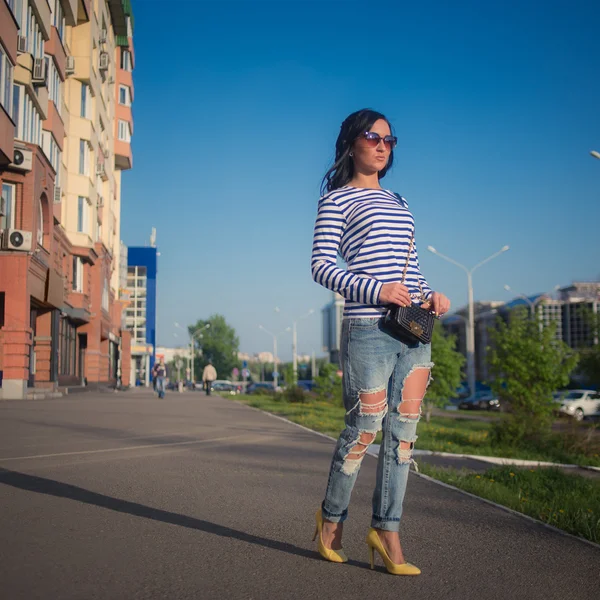 Piękna brunetka dziewczynka idzie ulicami miasta. w podarte dżinsy i kiecka — Zdjęcie stockowe