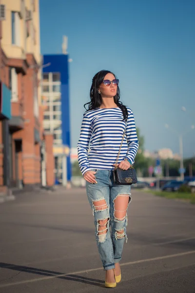 Beautiful brunette girl walks through the city streets. in torn jeans and frock — Stock Photo, Image