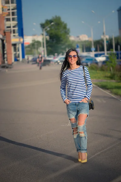 Schöne brünette Mädchen geht durch die Straßen der Stadt. in zerrissenen Jeans und Gehrock — Stockfoto