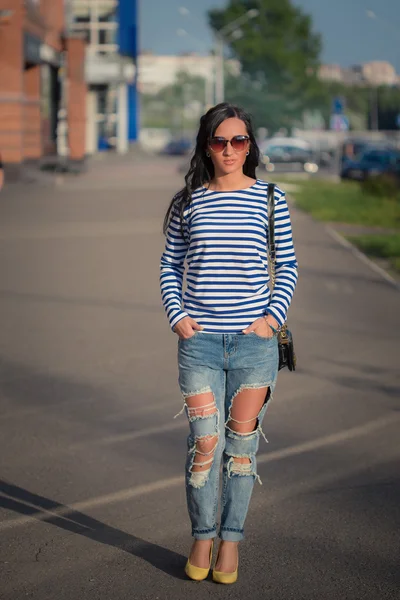 Linda menina morena caminha pelas ruas da cidade. em jeans rasgados e vestido — Fotografia de Stock