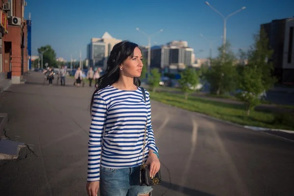 Hermosa chica morena camina por las calles de la ciudad. en vaqueros rasgados y vestido —  Fotos de Stock