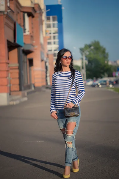 Schöne brünette Mädchen geht durch die Straßen der Stadt. in zerrissenen Jeans und Gehrock — Stockfoto