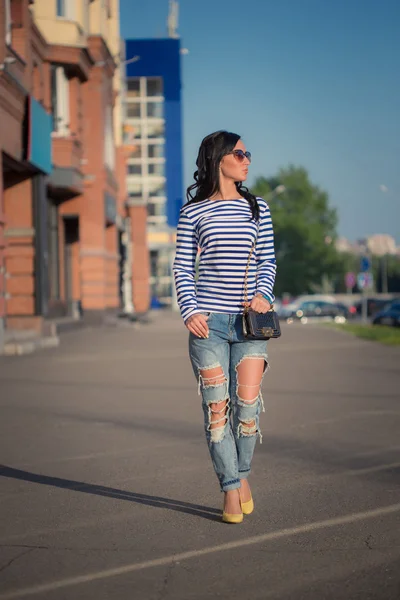 Linda menina morena caminha pelas ruas da cidade. em jeans rasgados e vestido — Fotografia de Stock