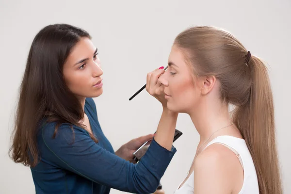 Maquillador haciendo maquillaje de una hermosa joven — Foto de Stock