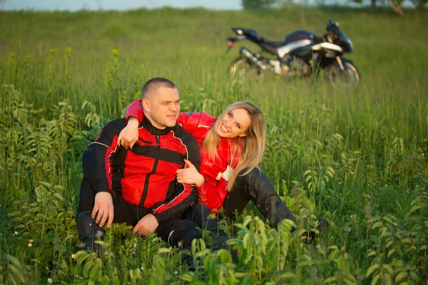 Biker girl and man sitting on the grass near a motorcycle — Zdjęcie stockowe