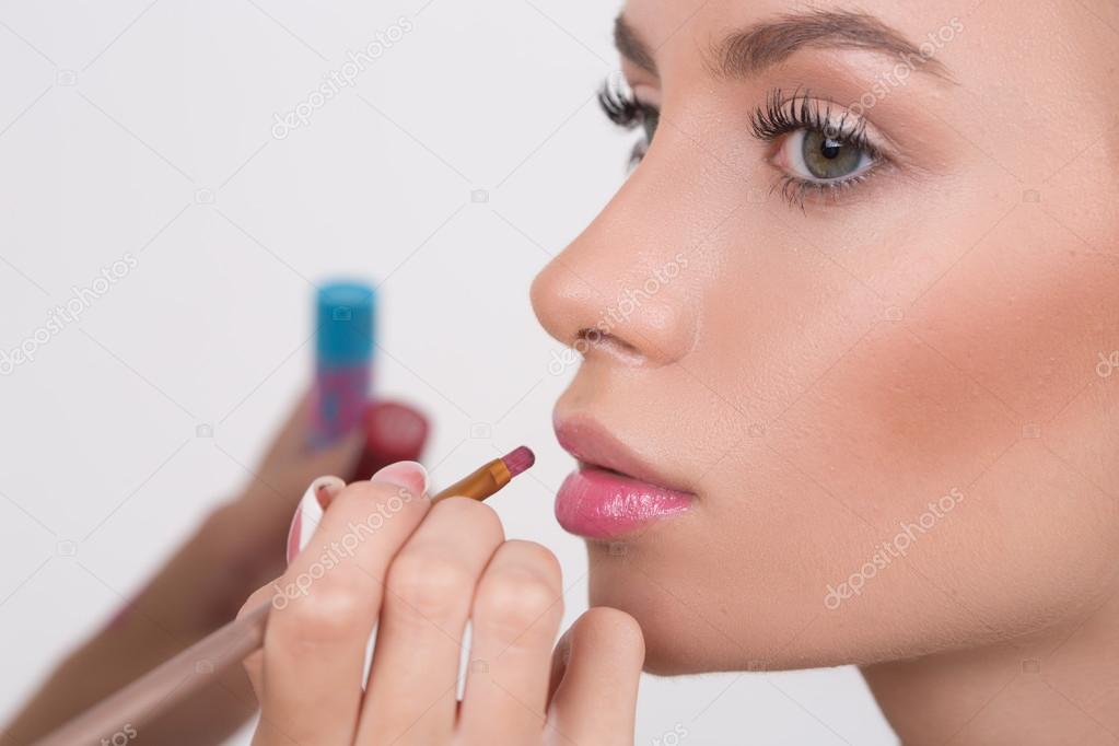 Makeup artist applies lipstick. Beautiful woman face. 