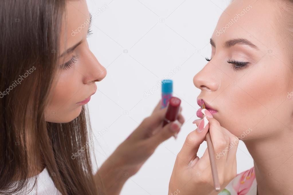 Makeup artist applies lipstick. Beautiful woman face. 