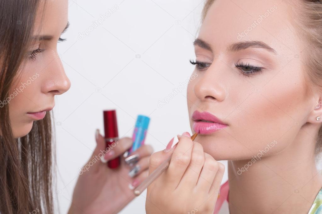 Makeup artist applies lipstick. Beautiful woman face. 