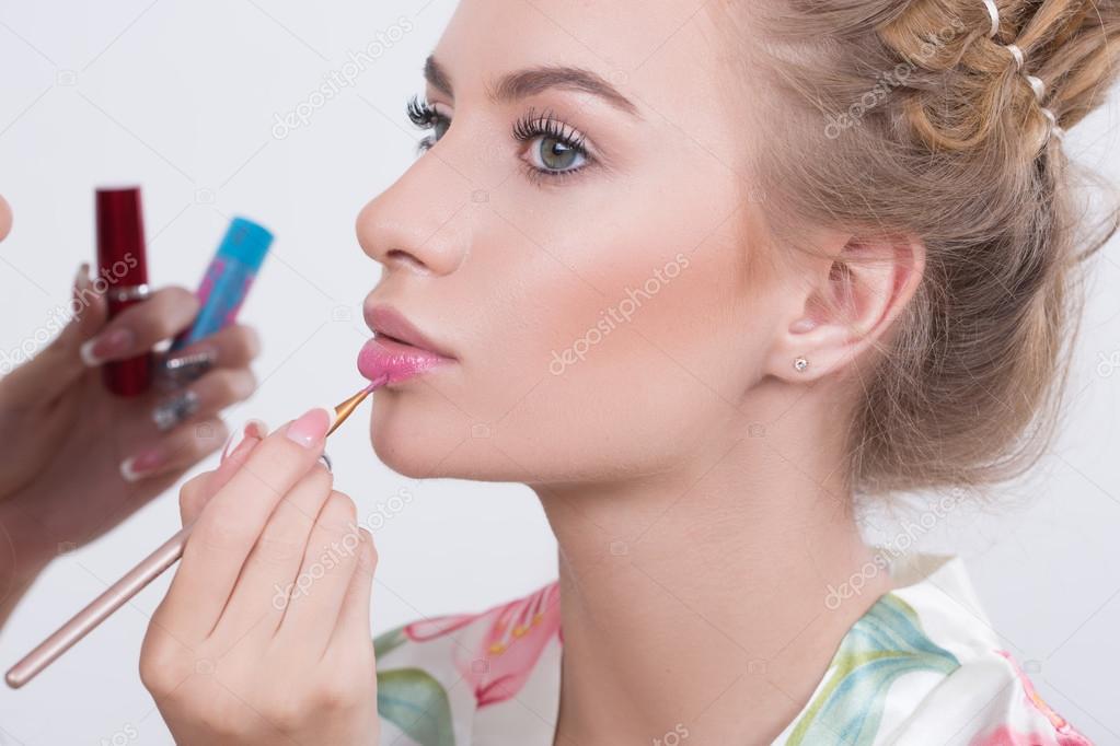 Makeup artist applies lipstick. Beautiful woman face. 